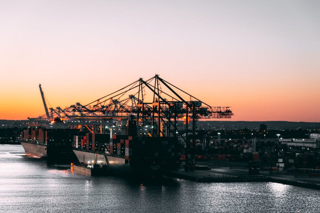 A serene view of cargo ships and cranes at a harbor during sunset, highlighting maritime industry.