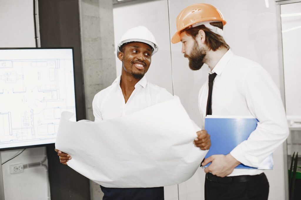 Two architects in hard hats discuss blueprints in a modern office setting, highlighting teamwork and planning.